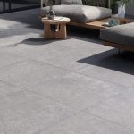Contemporary outdoor patio with grey Tuscany porcelain paving, featuring a textured stone effect and styled with modern wooden garden furniture.