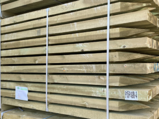 A large stack of pressure-treated timber fence posts with pointed ends, secured with plastic strapping.